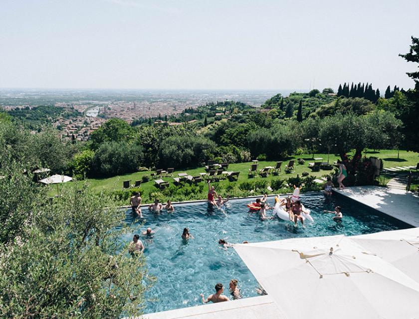 Piscina con vista panoramica sulla città, circondata da alberi e arredi da esterno.