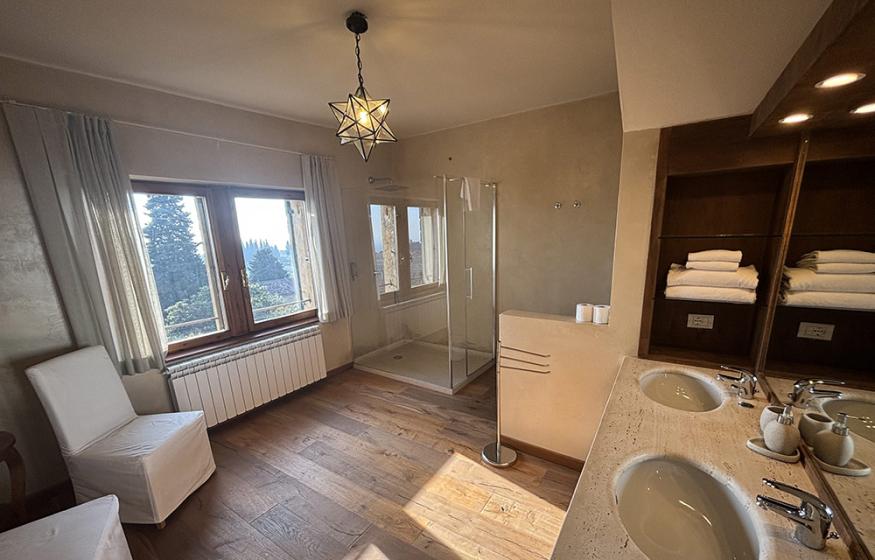 Elegante bagno con doppio lavabo, doccia e vista panoramica su alberi.