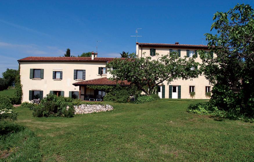 Casa di campagna con giardino verde, alberi e cielo blu.