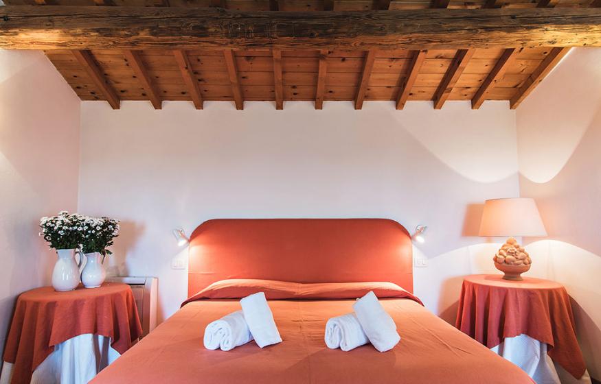 Camera accogliente con letto matrimoniale, travi in legno e decorazioni in tonalità arancione.