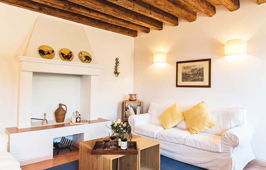 Soggiorno accogliente con camino, divano bianco, travi in legno e decorazioni rustiche.