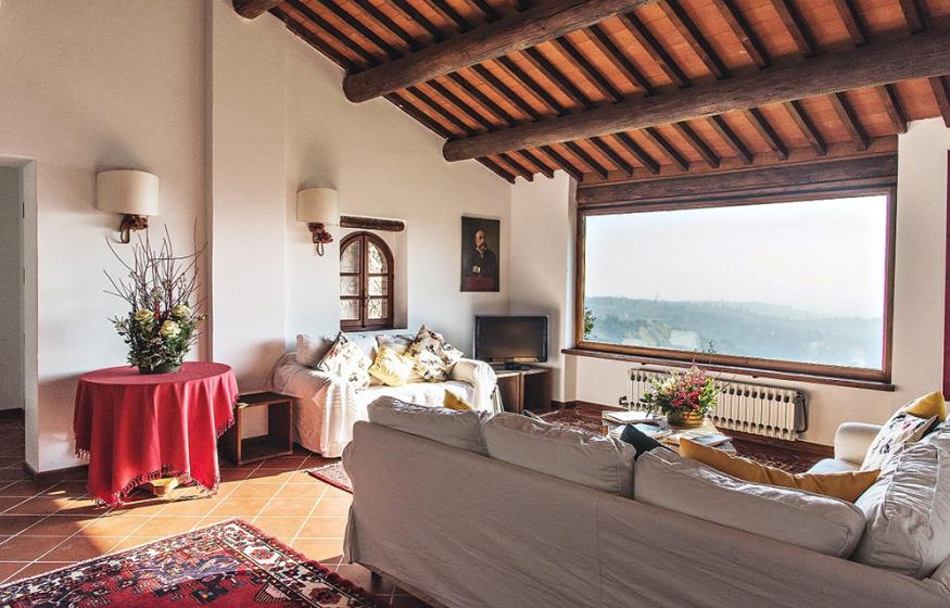 Soggiorno elegante con travi a vista, ampio finestrone e arredi accoglienti.