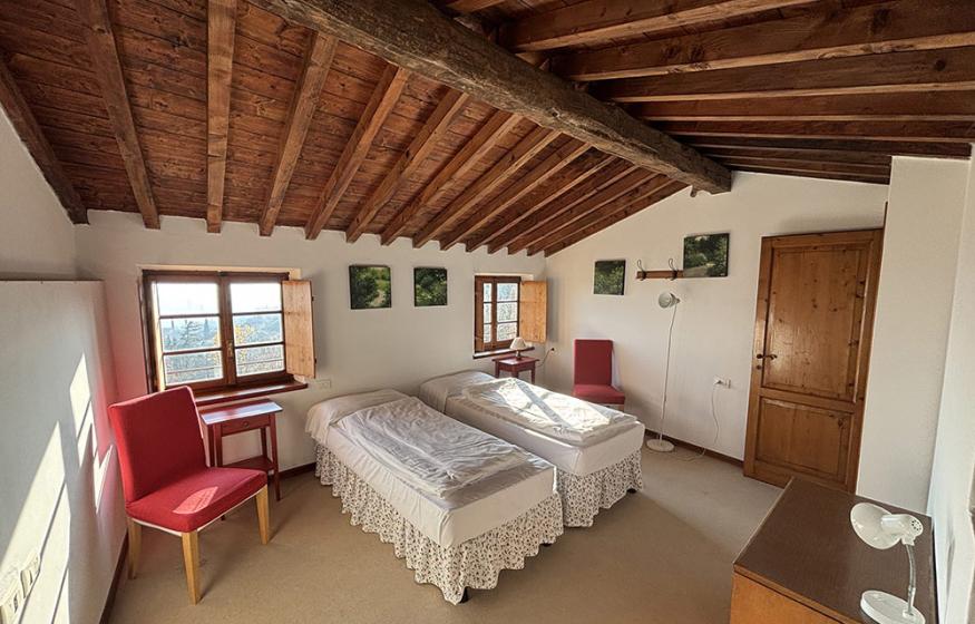 Camera rustica con letti singoli, soffitto in legno e arredi semplici.