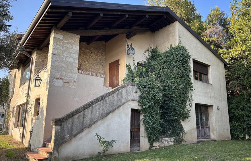 Casa in pietra con edera rampicante, scala esterna e tetto spiovente.