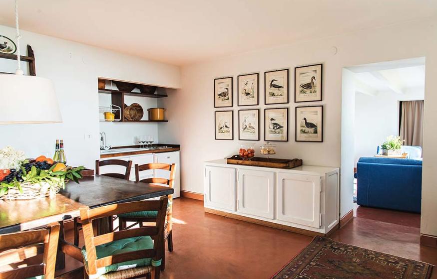 Sala da pranzo luminosa con tavolo in legno, quadri di uccelli e arredi rustici.