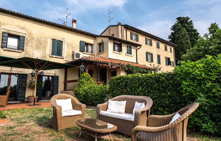 Cortile con mobili in vimini, ombrellone e edificio storico sullo sfondo.
