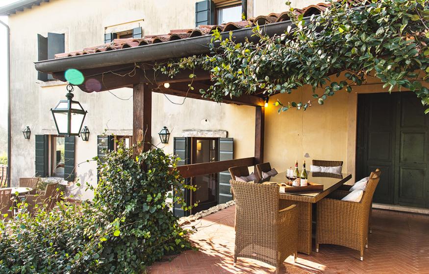 Terrazza accogliente con tavolo in vimini, piante rampicanti e illuminazione calda.